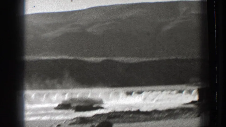 1939 Washington 8mm frame showing a dam spillway, falling water, foreground rocks, and a dark hillside through a vintage film border.