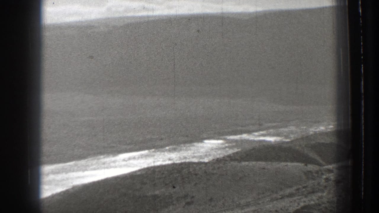 1939 Washington 8mm frame showing an aerial view over a shoreline or water edge with rolling hills and dark edge shadows.