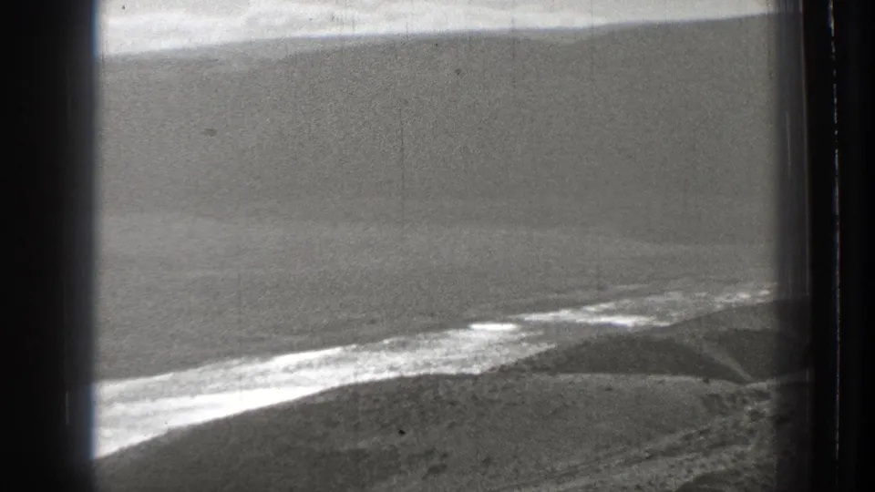 1939 Washington 8mm frame showing an aerial view over a shoreline or water edge with rolling hills and dark edge shadows.