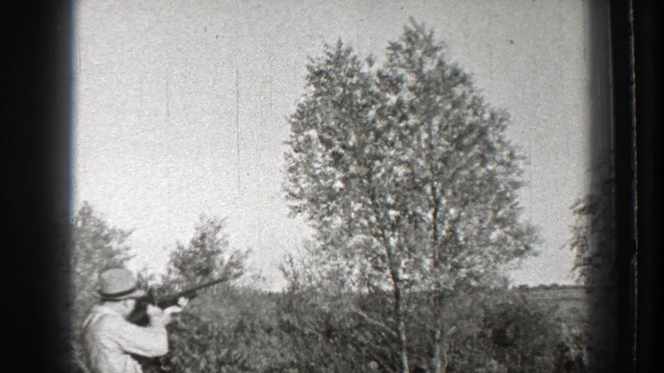 A man in a brimmed hat aims a shotgun across a grassy Washington field in 1939 home-movie footage.