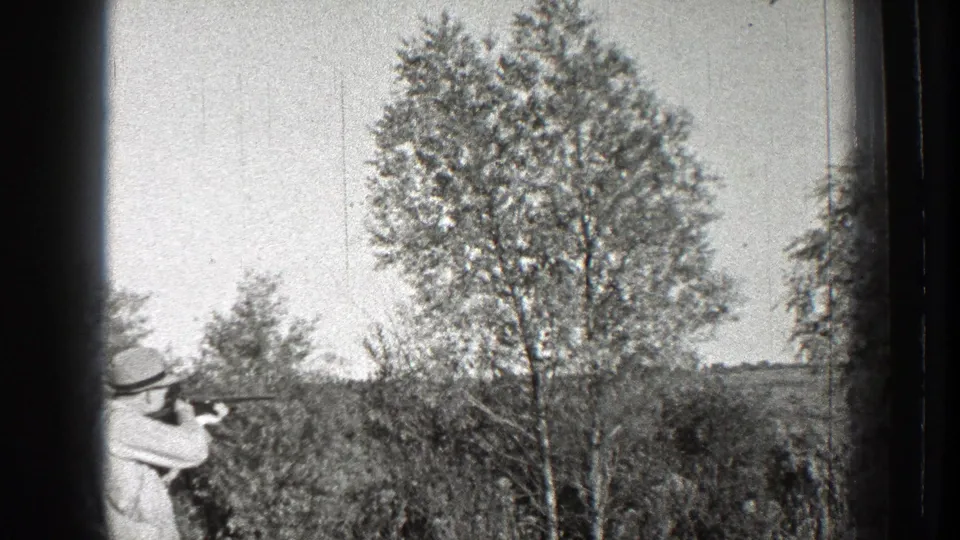 A hunter in 1939 Washington footage points a shotgun toward the trees as smoke appears near the barrel.