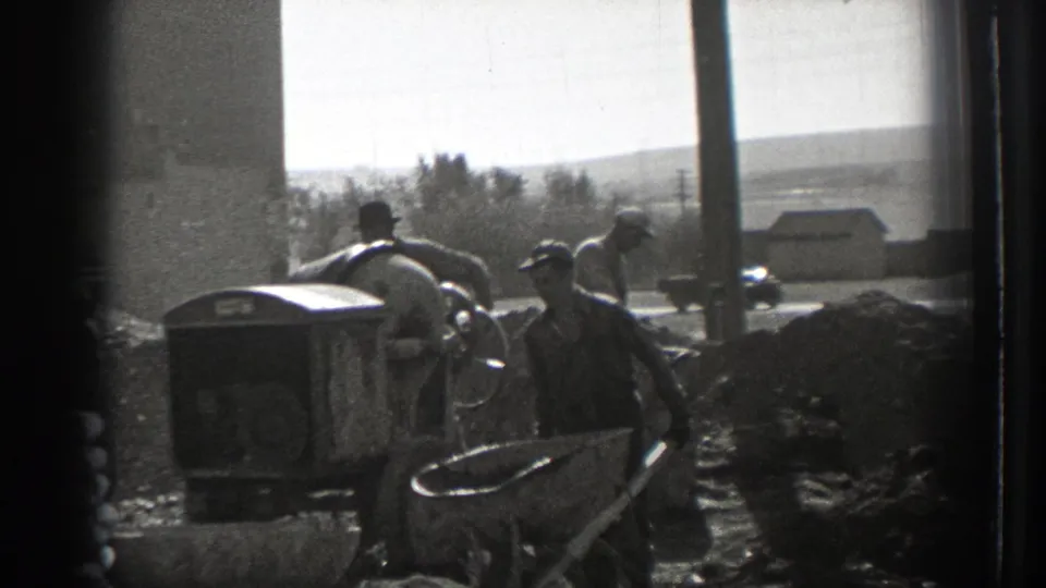 1939 Washington 8mm frame showing men in caps and work clothes near a concrete mixer, wheelbarrows, and aggregate piles.