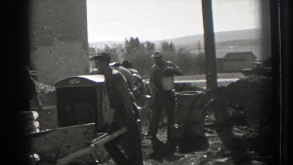 Workers at a Washington construction site appear beside a mixer, wheelbarrows, and rough material piles in a bright 1939 home-movie frame.