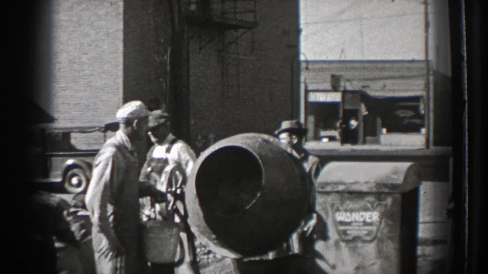 Men in caps and overalls stand near a mixer, a large barrel-like drum, and bagged material at the Washington construction site.