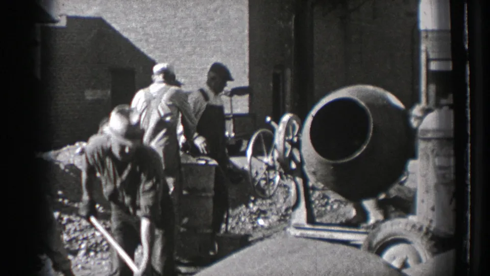 A worker shovels in the foreground as other men move around the cement mixer at the 1939 Washington industrial worksite.