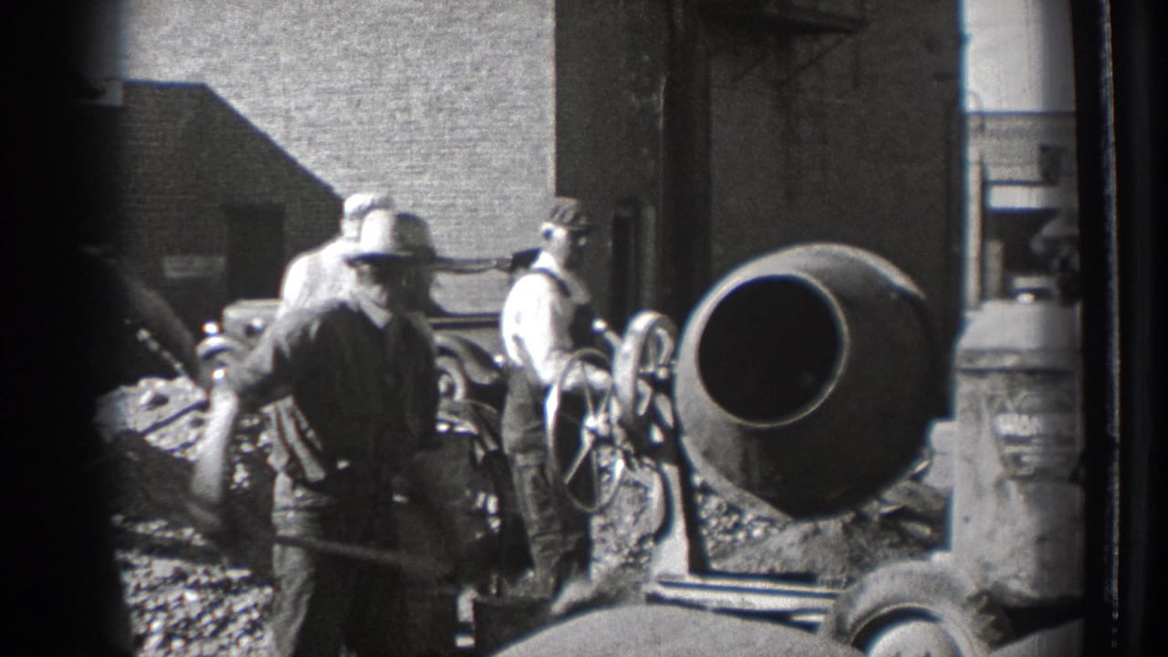 Men in work clothes stand near shovels and a cement mixer at an outdoor construction site.