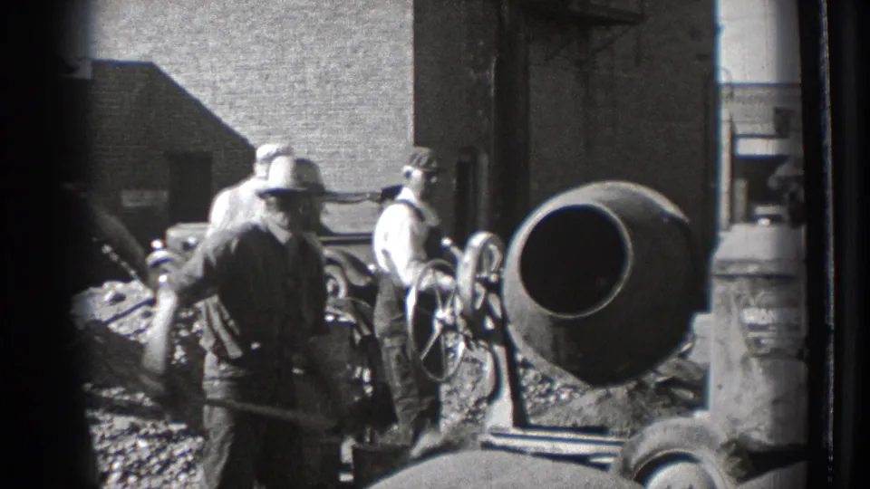 Washington 1939 home-movie frame showing men in hats and work clothes around shovels and a cement mixer beside brick buildings.