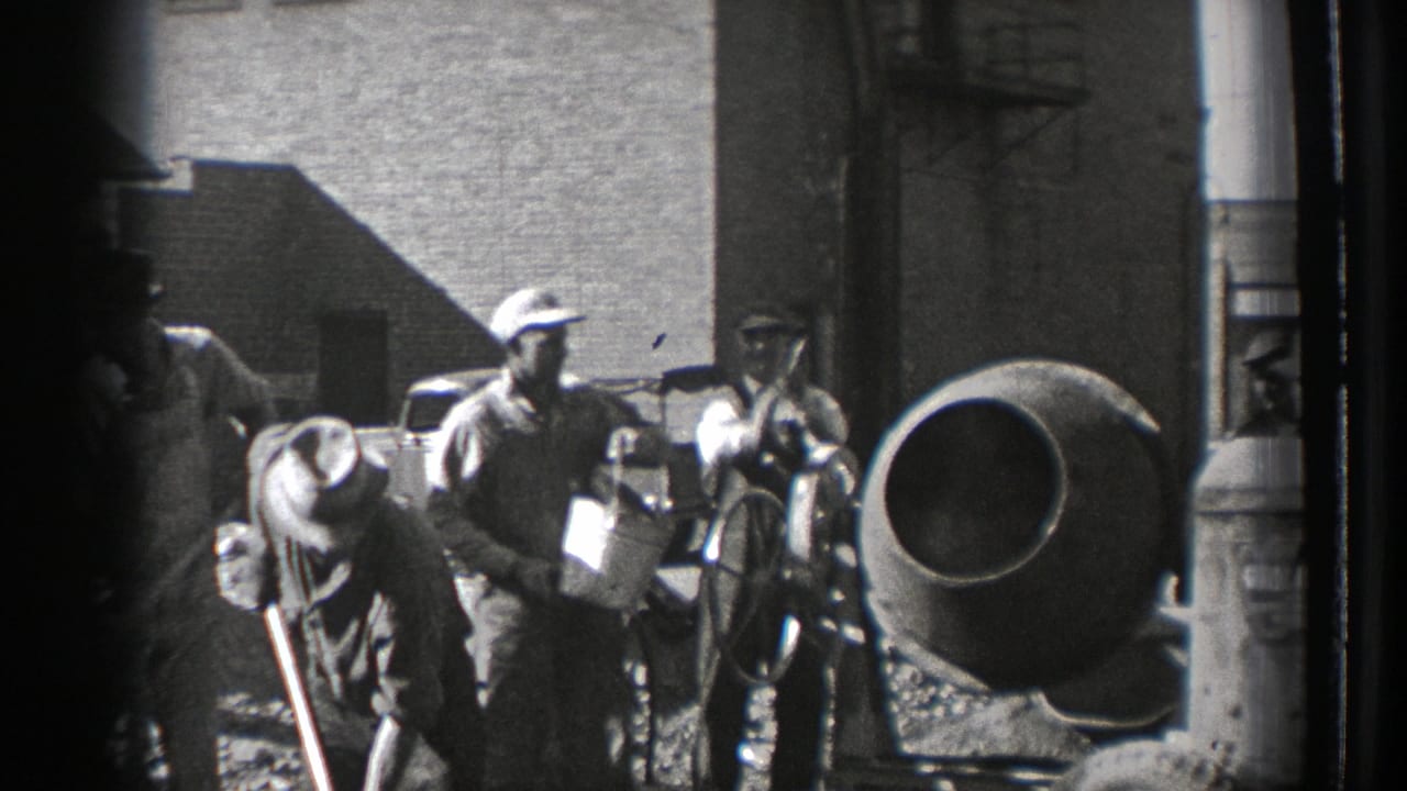 Several men work around a cement mixer, with one holding a container and others nearby.