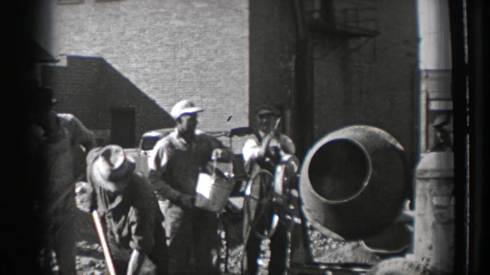 Washington 1939 frame with workers clustered around a wheeled cement mixer, hand tools, and brick industrial buildings.