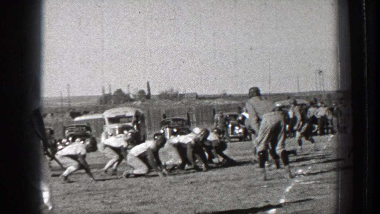 1939 Washington home-movie frame showing football players at the line of scrimmage with parked cars along the sideline.