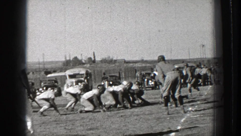 1939 Washington home-movie frame showing football players at the line of scrimmage with parked cars along the sideline.