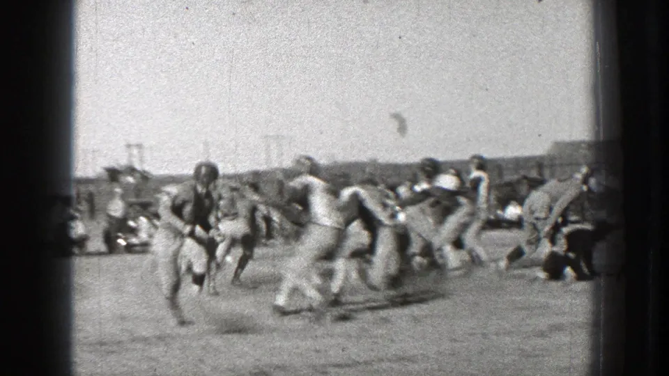 Football players run through a developing play on the dusty field as sideline figures watch in this 1939 Washington home-movie frame.