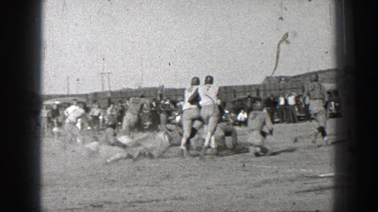 Helmeted players on a dusty field with spectators along the sideline.