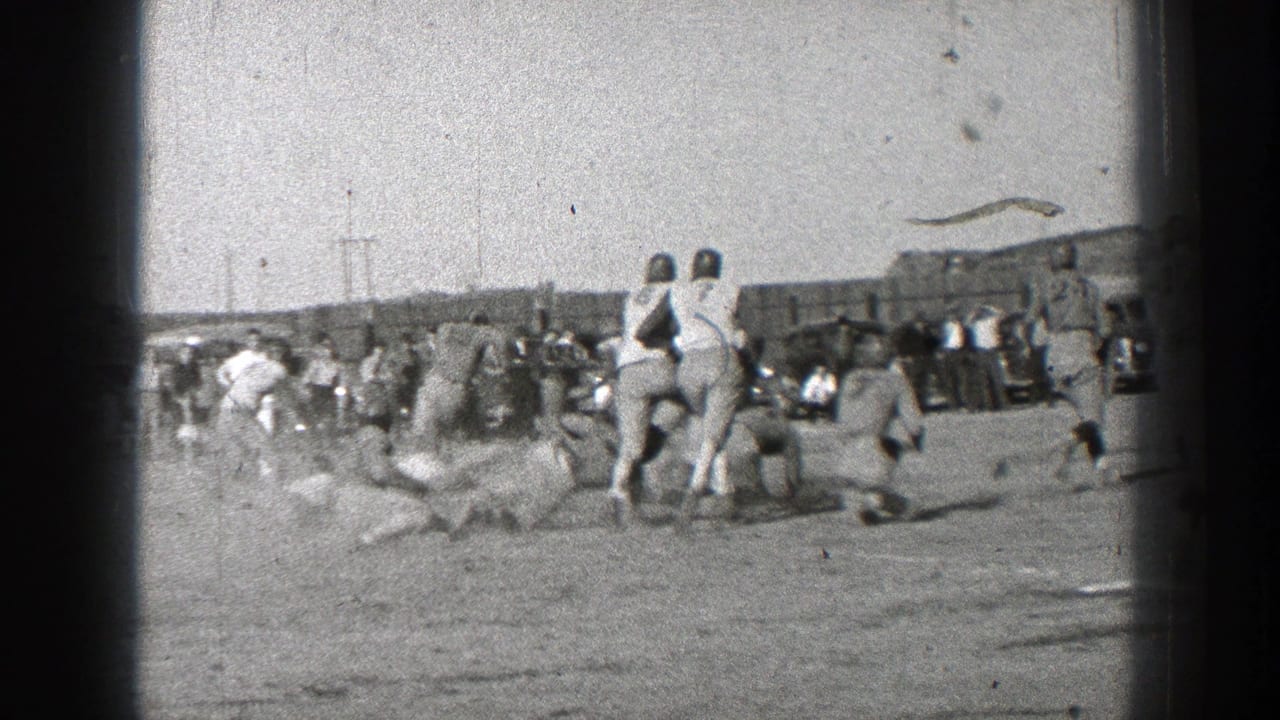 Players cluster near the sideline with spectators and field structures behind them.