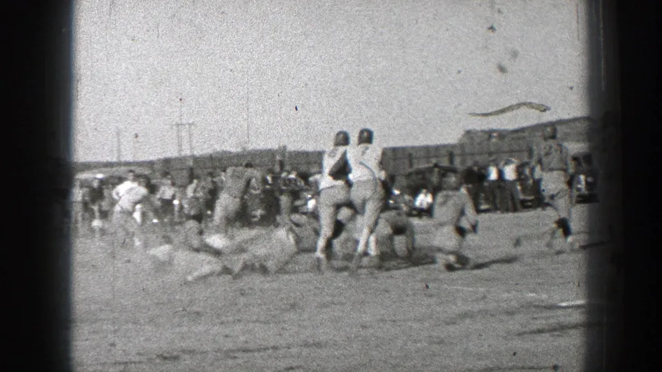 1939 Washington frame with players gathered near the sideline, spectators in the background, and a dusty open playing area.