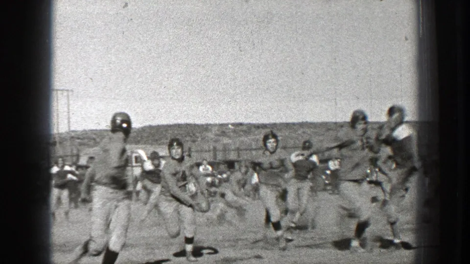 1939 Washington home-movie frame showing helmeted players running and a tackle or fall during an amateur field sport game.