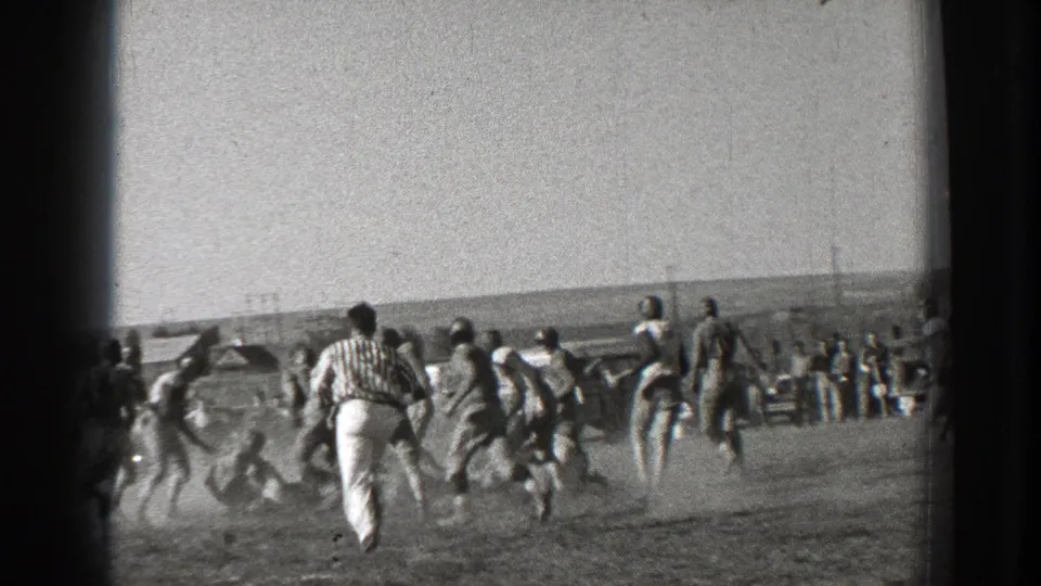 Washington 1939 home-movie frame showing football players in motion on an open field with spectators beyond the sideline.