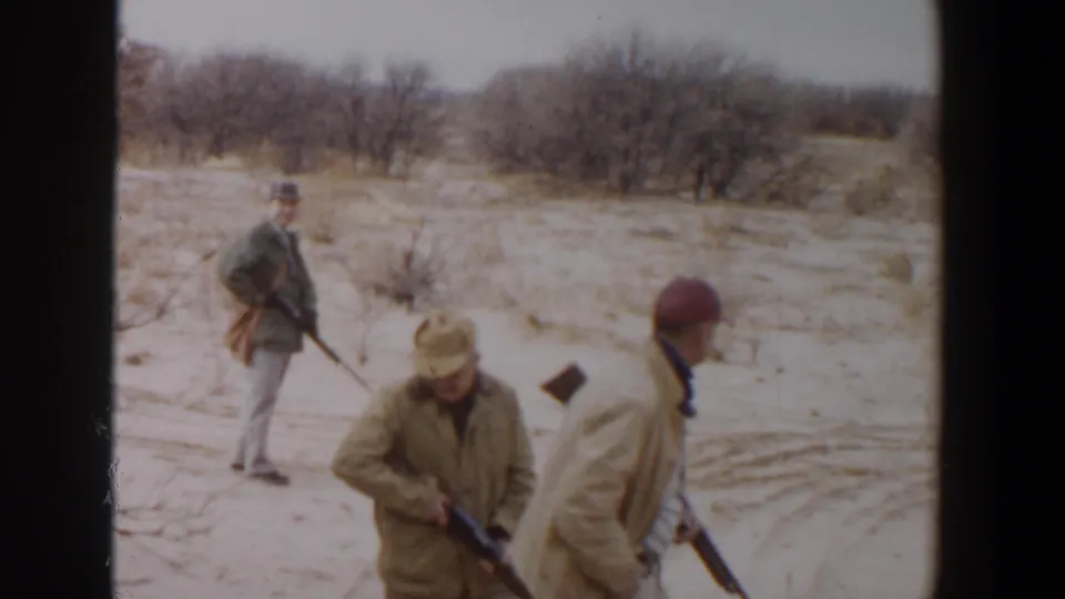 Three adult men with rifles are seen in a dry Lubbock brush field, with one turning toward the others near visible tire tracks.