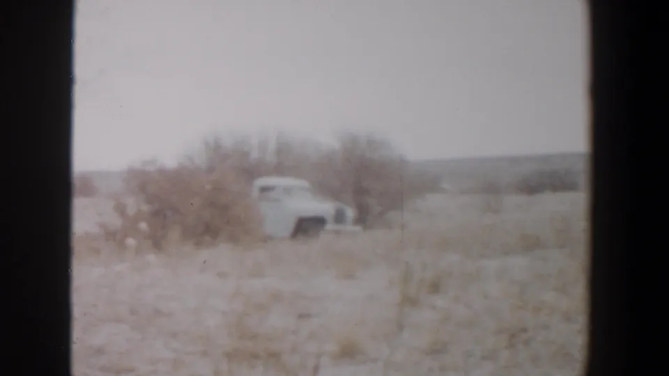 1956 Lubbock, Texas frame showing a distant light-colored vehicle or small trailer near brush and open rural land.