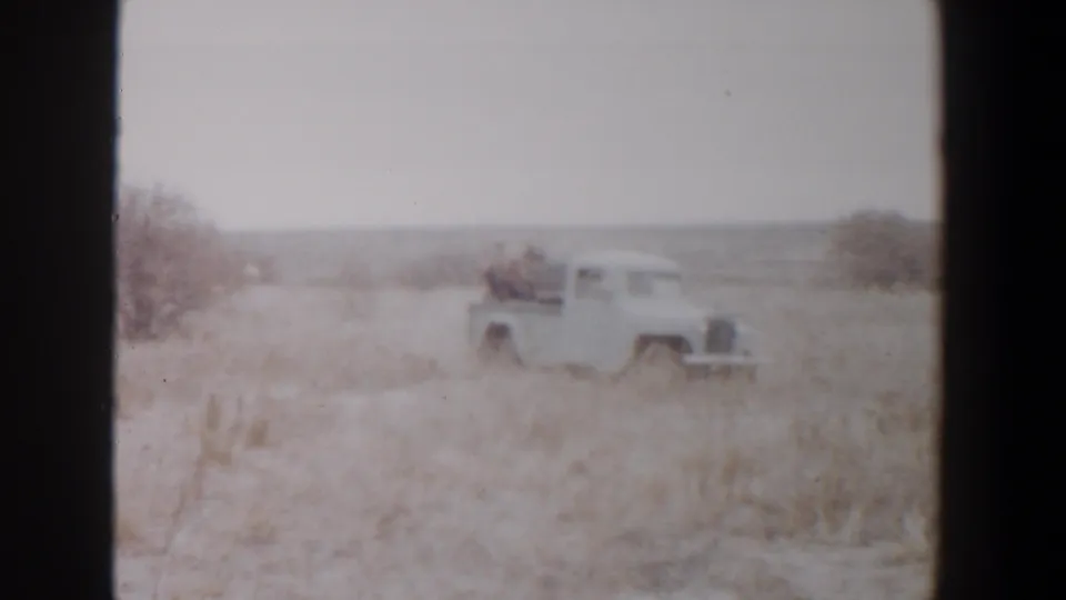 1956 rural Texas home-movie frame showing a white pickup and riders moving through dry grass with brush and a distant horizon.