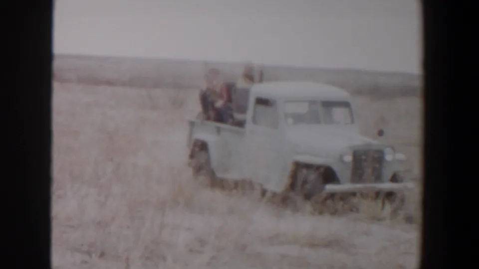 Closer 1956 Lubbock-area frame of the white pickup pushing through dry grass with riders seated in the open bed.