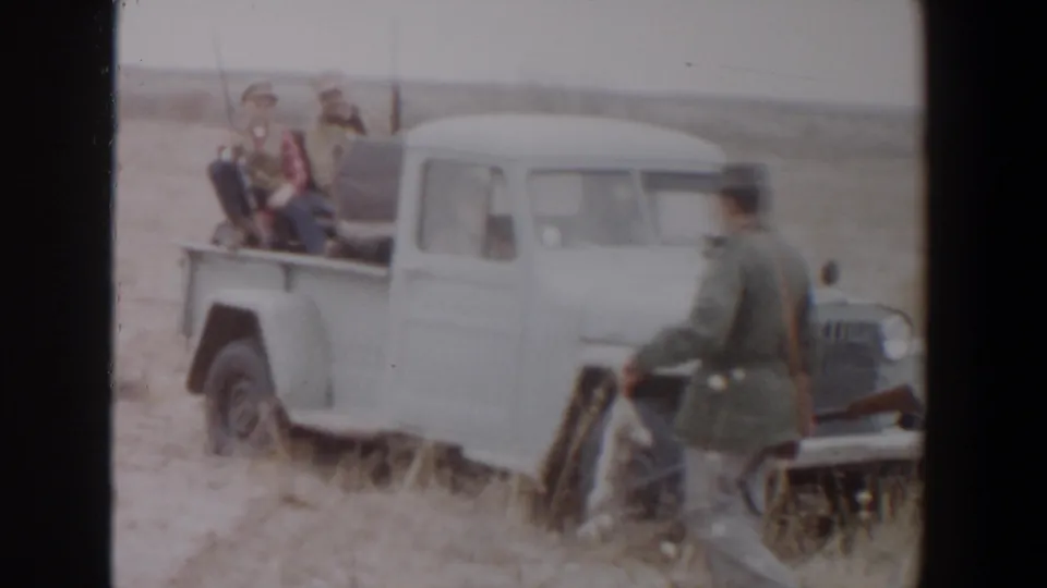 In the 1956 Lubbock hunting scene, a man in a jacket and hat walks near the white pickup while carrying a rifle.