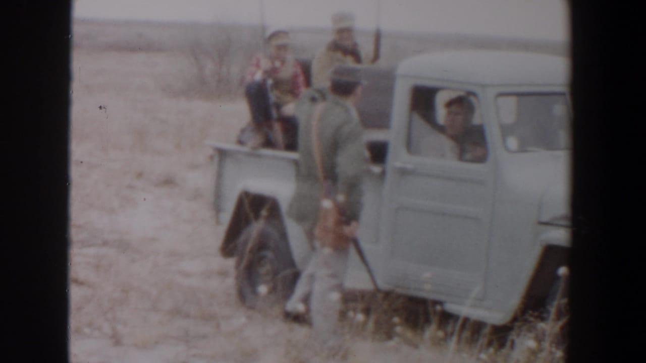 1956 Lubbock, Texas home-movie frame showing hunters around a light blue pickup truck in open brushland.