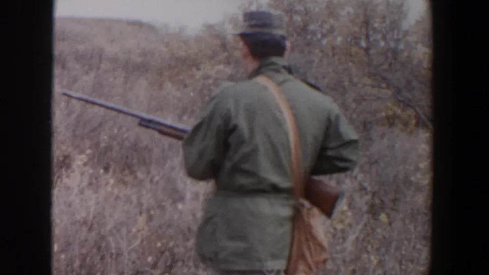 Rear view of a man with a rifle walking through dry Lubbock brush in the supplied 1956 8mm home movie.