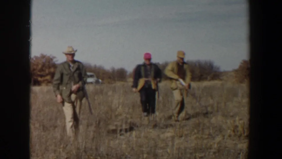 Three adult hunters in 1956 Lubbock, Texas, walk through dry grass with long guns and hats.