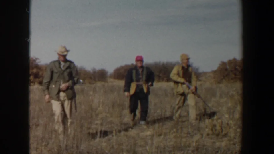 Three adult hunters in a dry Lubbock field continue forward, one wearing a bright pink cap.