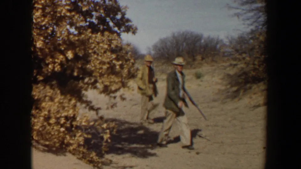 In 1950s Lubbock, Texas home-movie footage, two hunters walk past a tree and dry brush while carrying rifles.