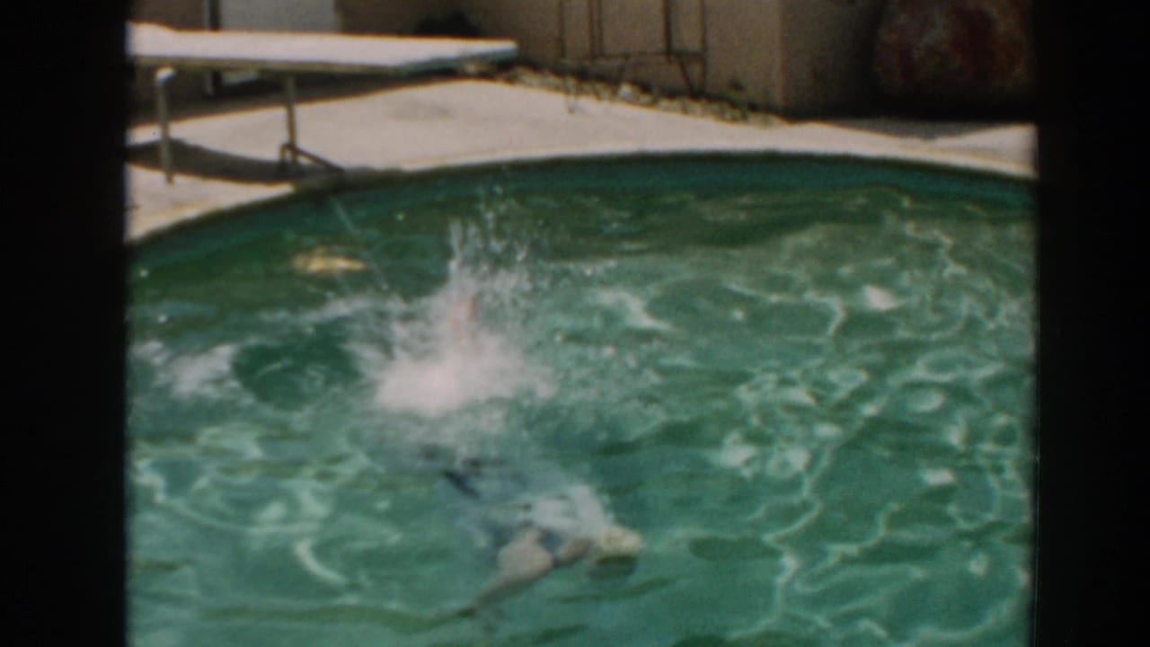 Woman enters a backyard pool from a diving board, creating a splash in the water.