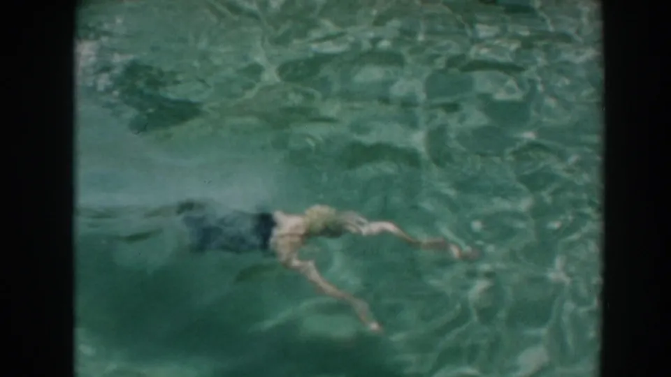 A swimmer glides underwater in the North Hollywood backyard pool, seen through rippled 8mm color footage from 1961.