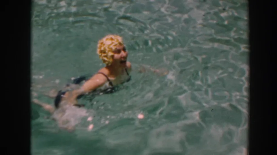 A woman in a dark swimsuit swims at the surface of the North Hollywood backyard pool in supplied 1961 home-movie footage.