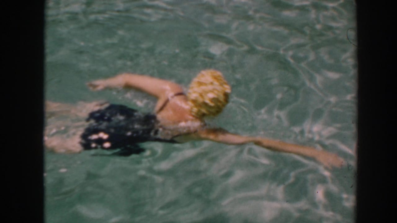 Woman in a yellow swim cap swims across a backyard pool.