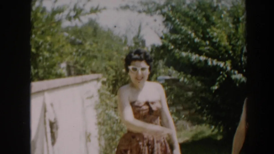 In the 1961 backyard scene, the woman in a patterned dress moves near a low wall, with the man partly cropped at the edge.