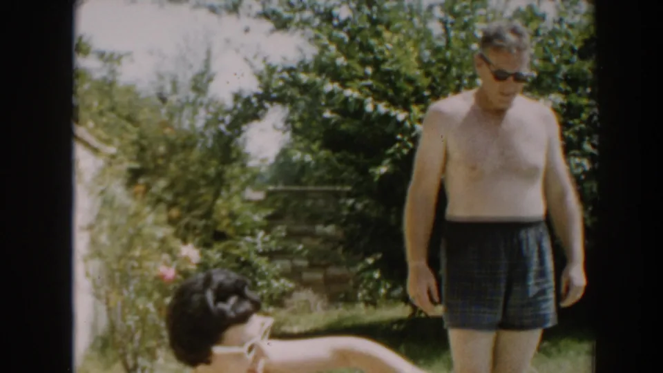In the North Hollywood backyard, the man stands upright in swim trunks as the woman in white sunglasses bends near the bottom of the frame.