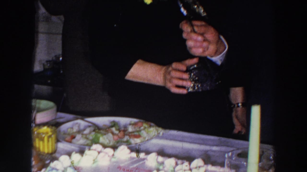 Party table with salad, cake pieces, candles, and guests gathered nearby.