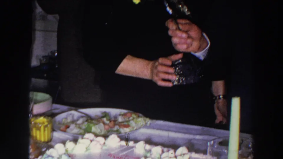 1966 Madison home-movie frame showing an indoor celebration table with food, candles, and guests partly visible around it.