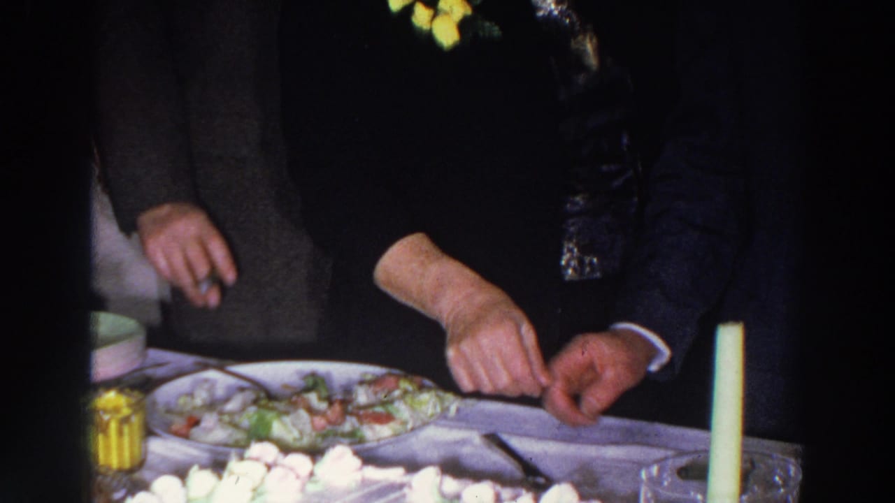 A woman with a yellow corsage cuts cake beside suited guests.
