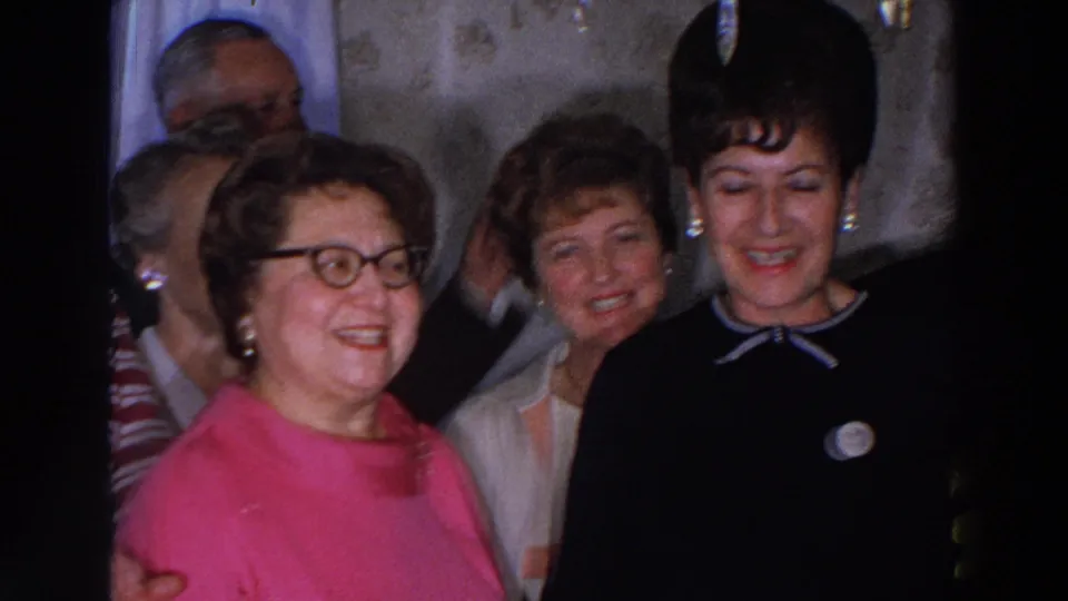 Women at a 1966 Madison, Wisconsin indoor gathering smile and appear to sing or speak, framed closely by the home-movie camera.