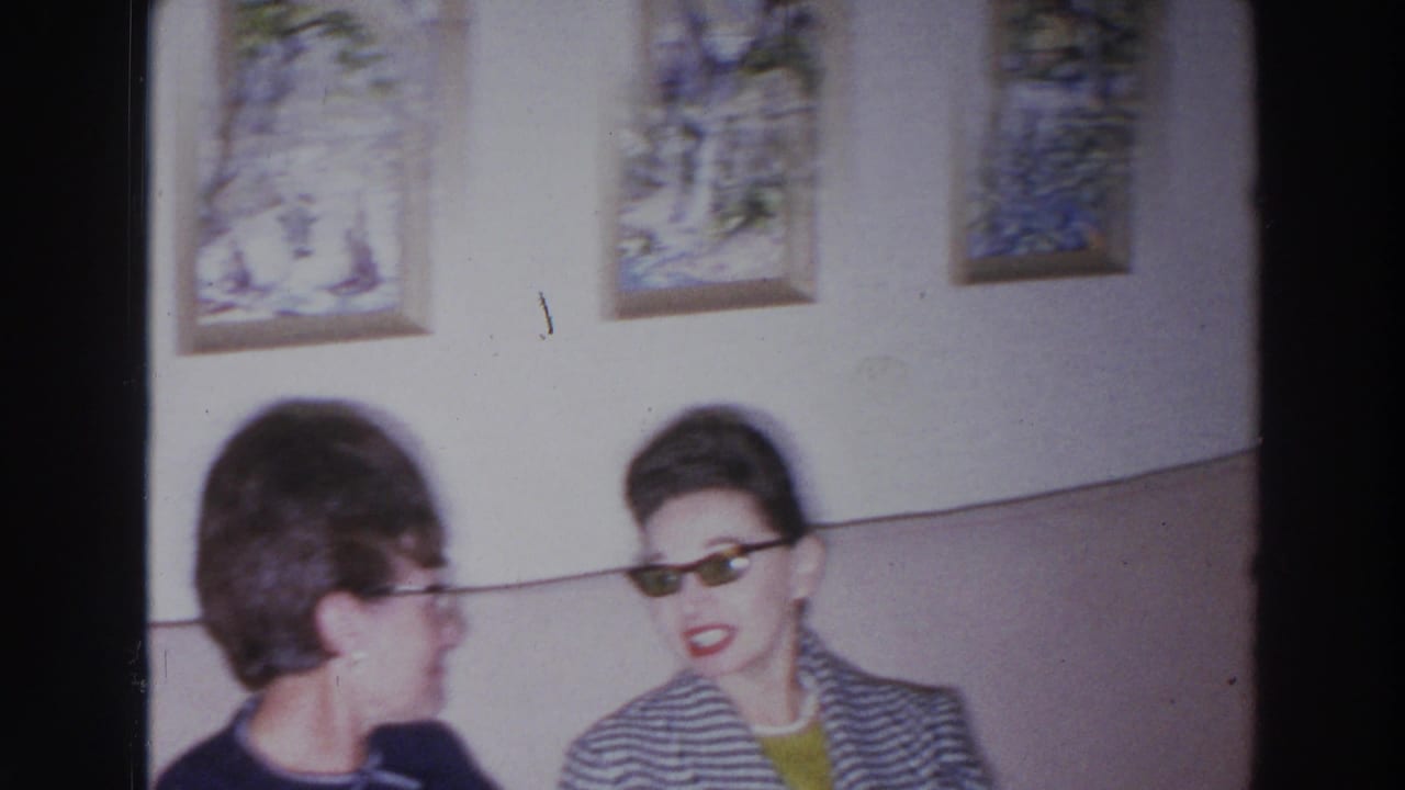 Two women sit on a couch beneath framed wall art in a living room.