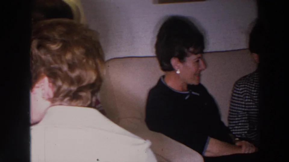 A 1966 home-movie frame shows a smiling woman on a beige couch, partly obscured by another seated person in the foreground.