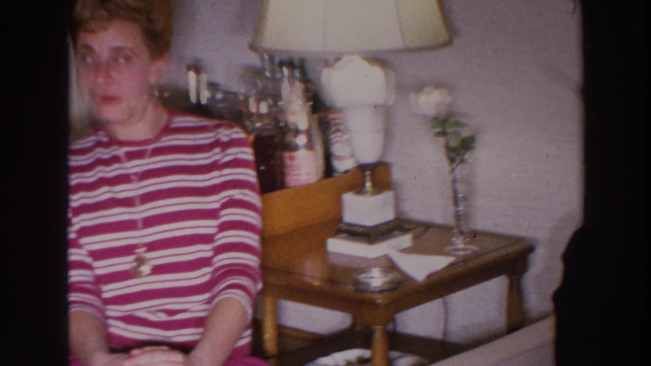 Woman in a red and white striped sweater sits near a lamp and side table in a living room.