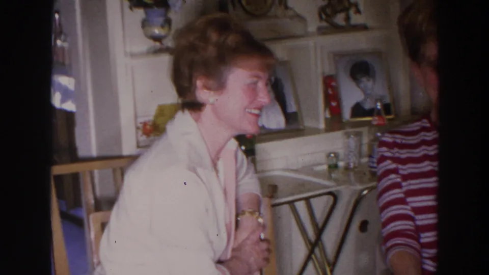In the Madison living-room footage, a woman in a light top laughs in profile beside another seated woman and framed portraits.