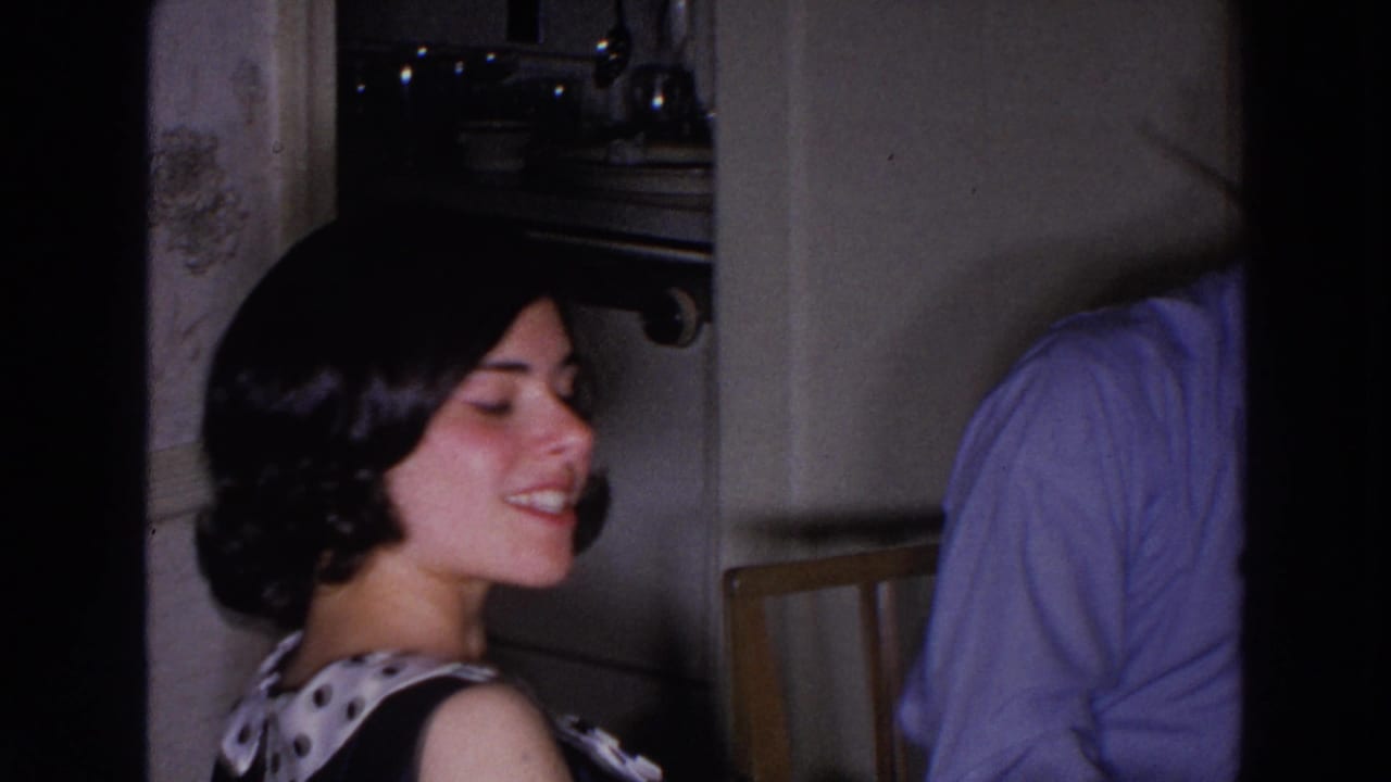 In a 1966 Madison home interior, a young woman in a polka-dot dress appears beside a man in a blue shirt near kitchen seating.