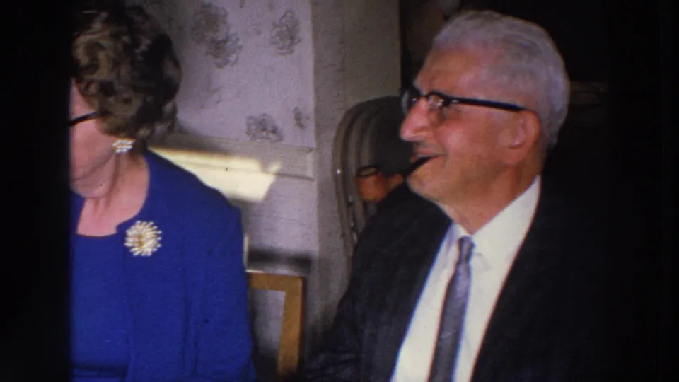 An elderly man in a suit and tie smiles beside the woman in blue during the 1966 Madison formal dinner gathering.