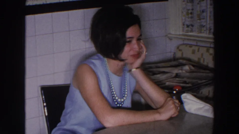 The woman returns to a quieter pose, hand against her cheek, seated at the counter in the Madison home kitchen footage.