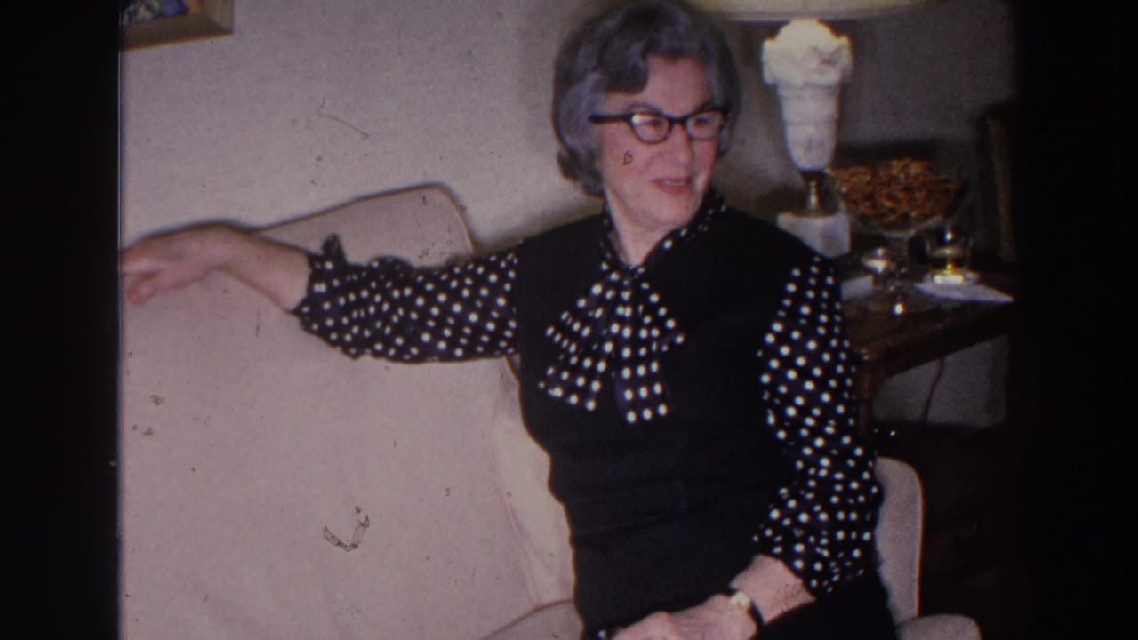 Woman in glasses sits on a sofa with her arm along the back in a living room.