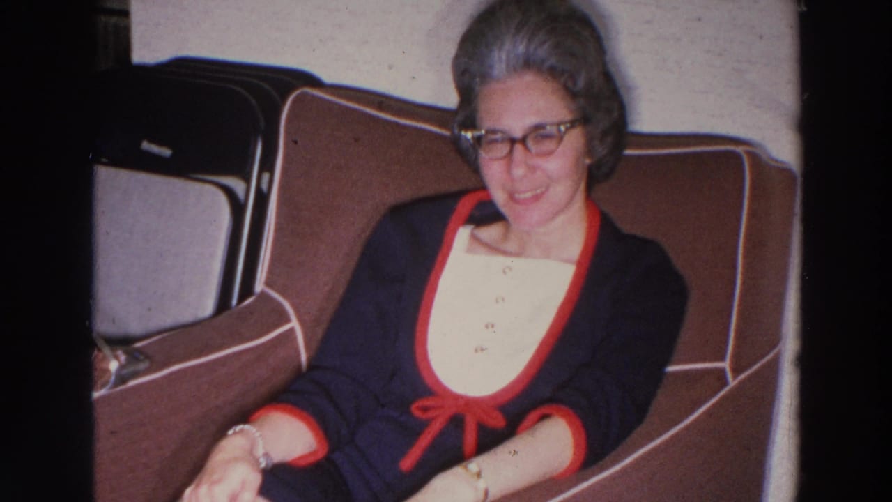 Woman with glasses seated in a brown upholstered chair, smiling toward the camera.